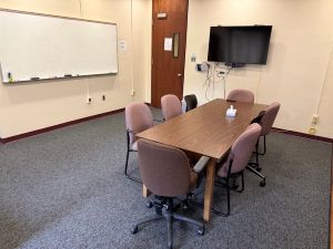CarsonRoom2 Conference room table with seating, wall-mounted TV, and whiteboard in the Carson Room